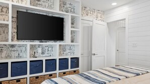 A bedroom with a large TV mounted on the wall, built-in storage with blue drawers, a bed with striped bedding, and a white door.