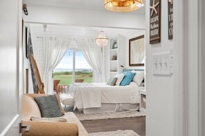 A bedroom with a bed, a chair, a table, and a view of the outdoors. - Hoopers Landing | Private Dock | Hot Tub (Fishing Creek)