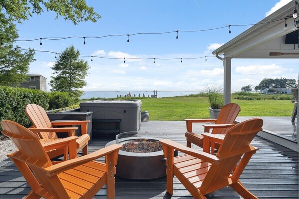 An outdoor deck with wooden chairs, a fire pit, and a hot tub.