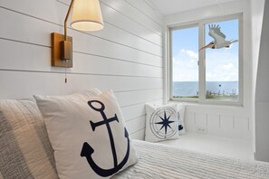 A bedroom with a bed, a window with a seagull decoration, and nautical-themed pillows.