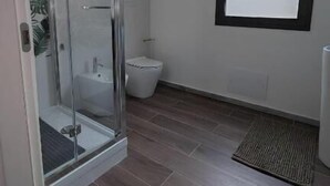 A bathroom with a glass shower enclosure, a toilet, and a window with a black frame.
