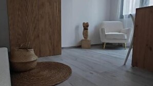 A room with a wooden floor, a white chair, a woven rug, and a decorative wooden piece.