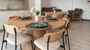 A modern dining area with a round wooden table, six chairs, and a vase with flowers.