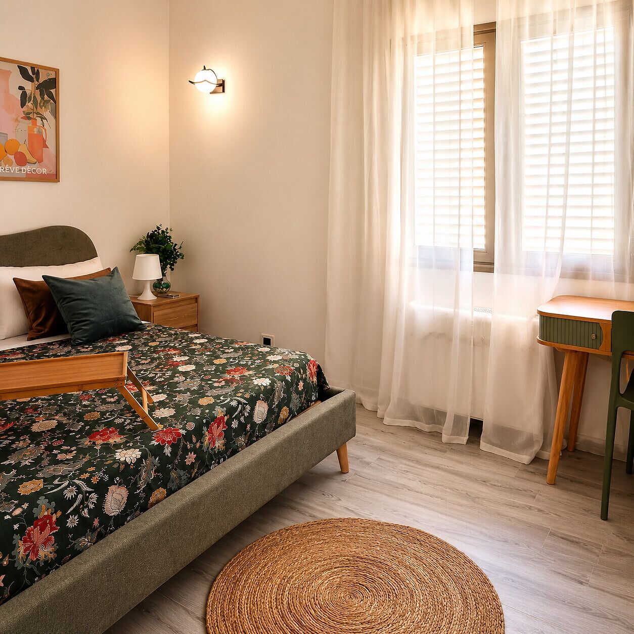 A bedroom with a bed, bedside table, lamp, and a window with sheer curtains.