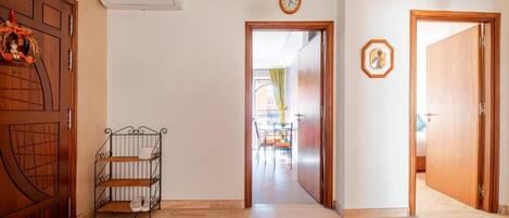 A hallway with a wooden door, a metal rack with shoes, a wall-mounted air conditioner, and a clock.