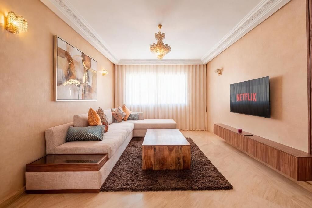 Uma sala de estar moderna com um sofá seccional, uma mesa de centro de madeira, uma TV montada na parede e um candelabro.