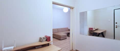 A room with a desk, a mirror, a sofa, and a door leading to another room.
