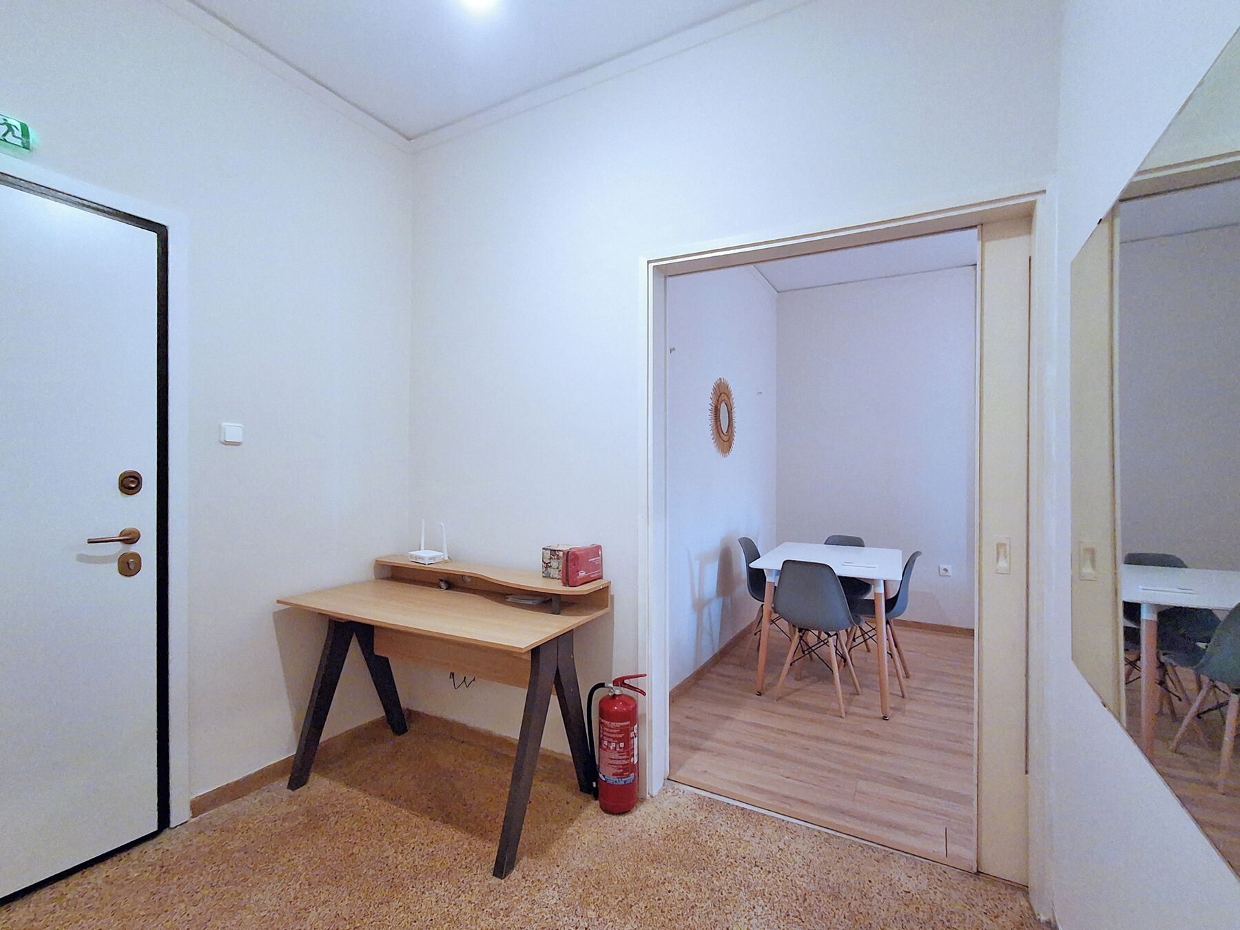 A room with a door, a desk, a chair, a small table, and a fire extinguisher.