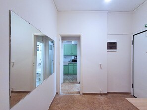 A narrow hallway with a mirrored wall, leading to a green kitchen area with cabinets and a microwave. - Comfortable Apt near Larissis Metro (Athina)