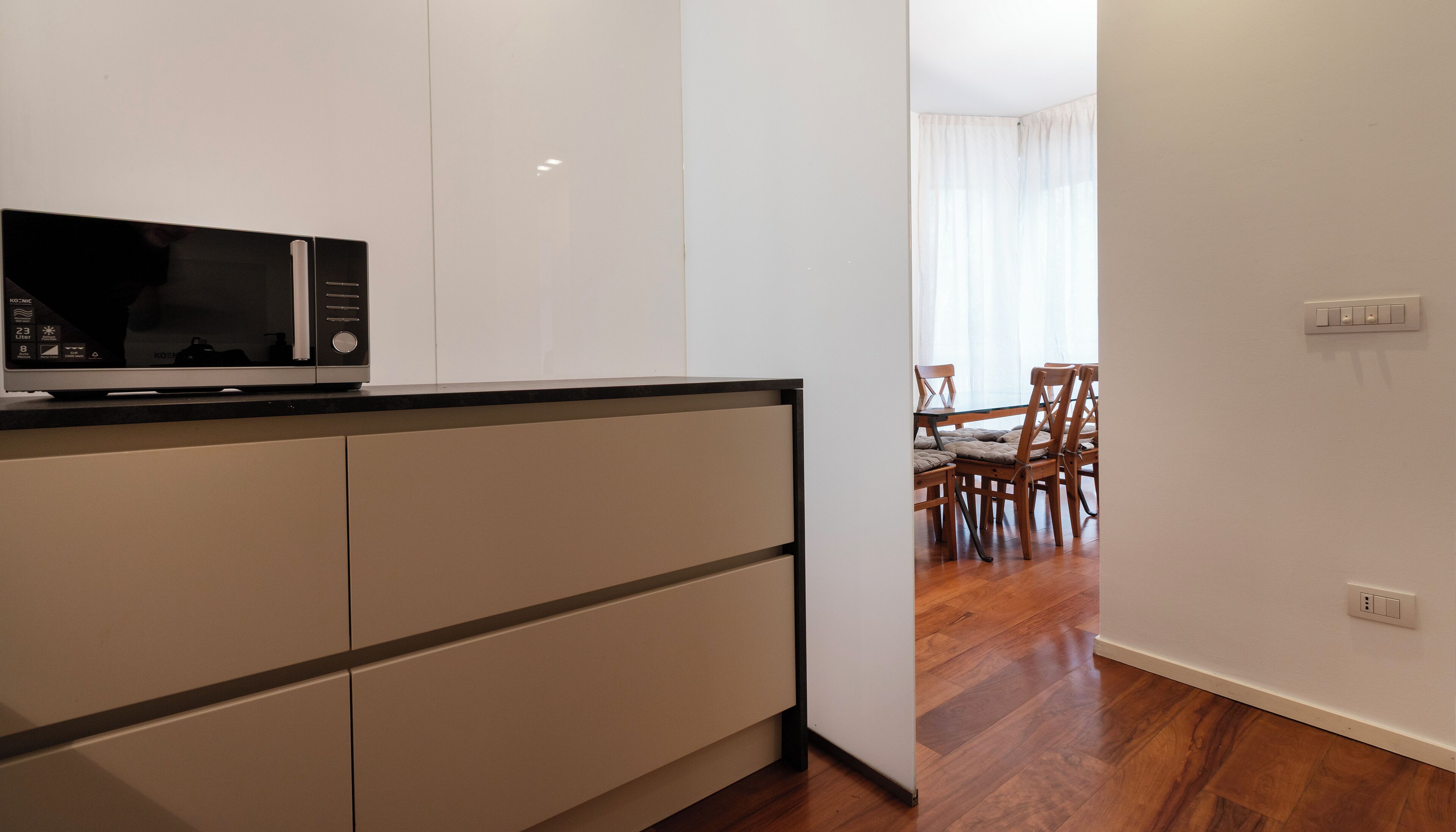 A modern kitchen with a microwave, cabinets, and a dining area with chairs and a table.