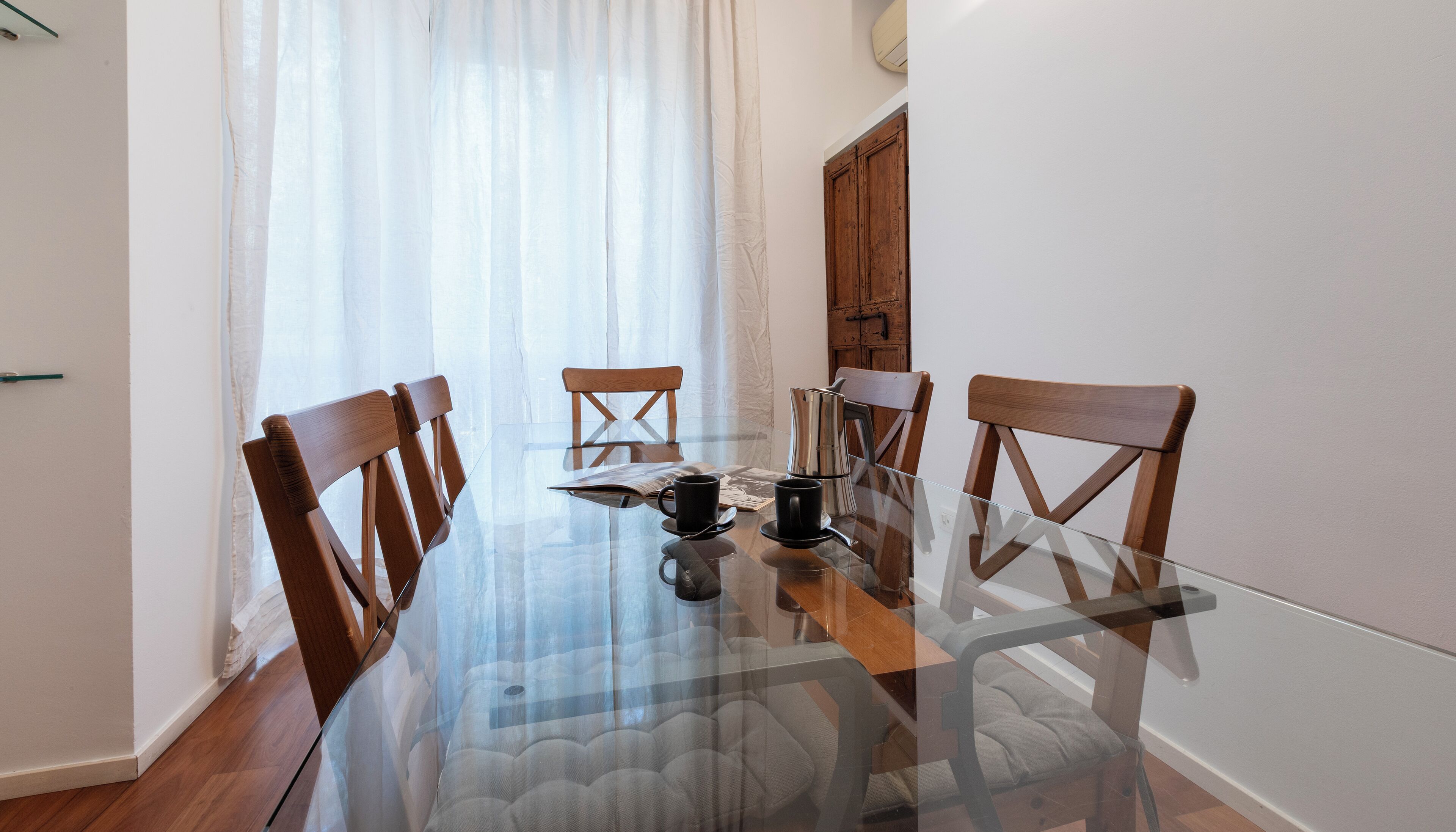 A dining area with a glass table, wooden chairs, and a coffee pot.