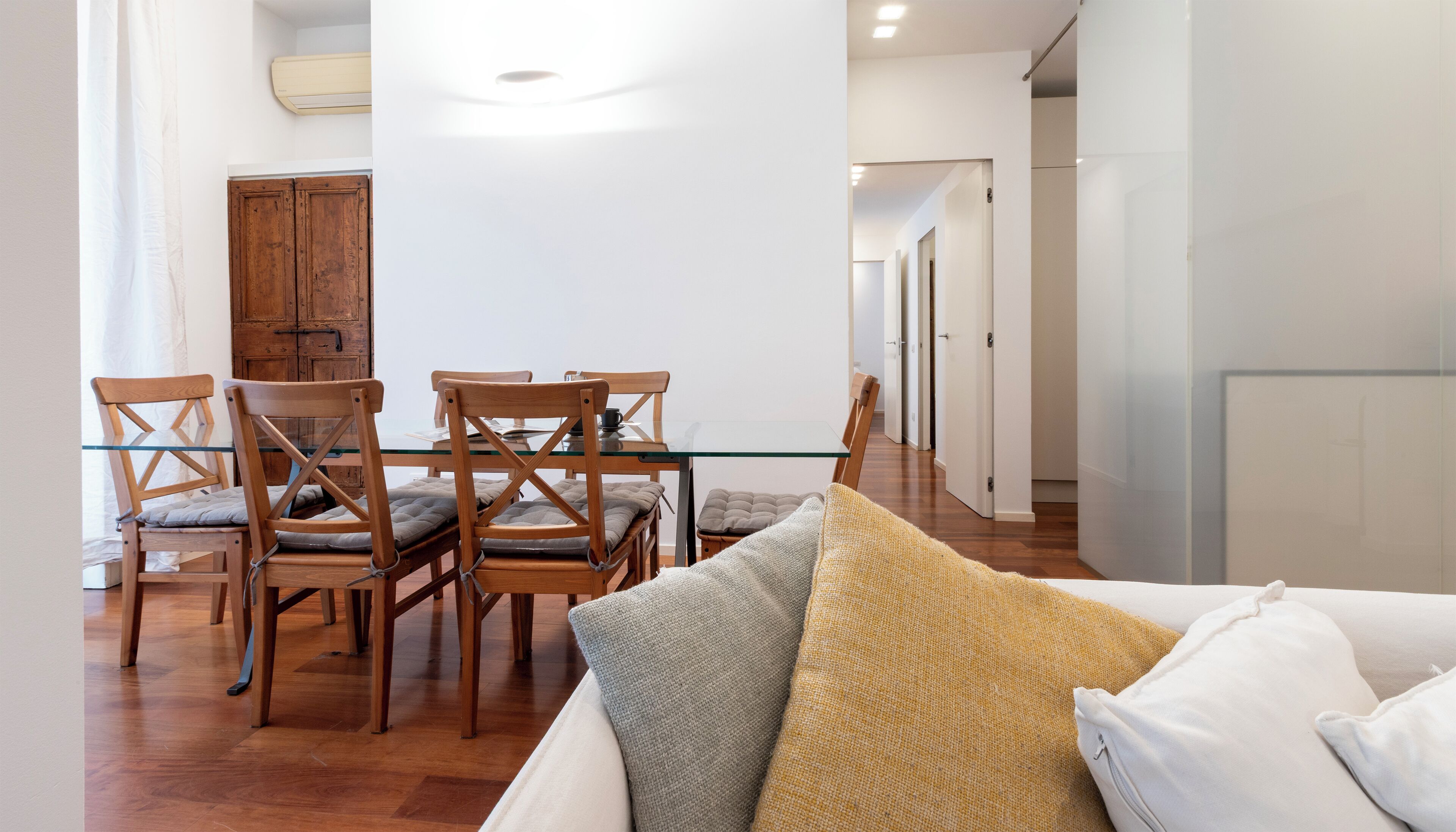 Una sala de estar moderna con una mesa de comedor de vidrio, sillas de madera y un sofá con cojines.