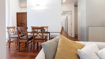 Una sala de estar moderna con una mesa de comedor de vidrio, sillas de madera y un sofá con cojines.