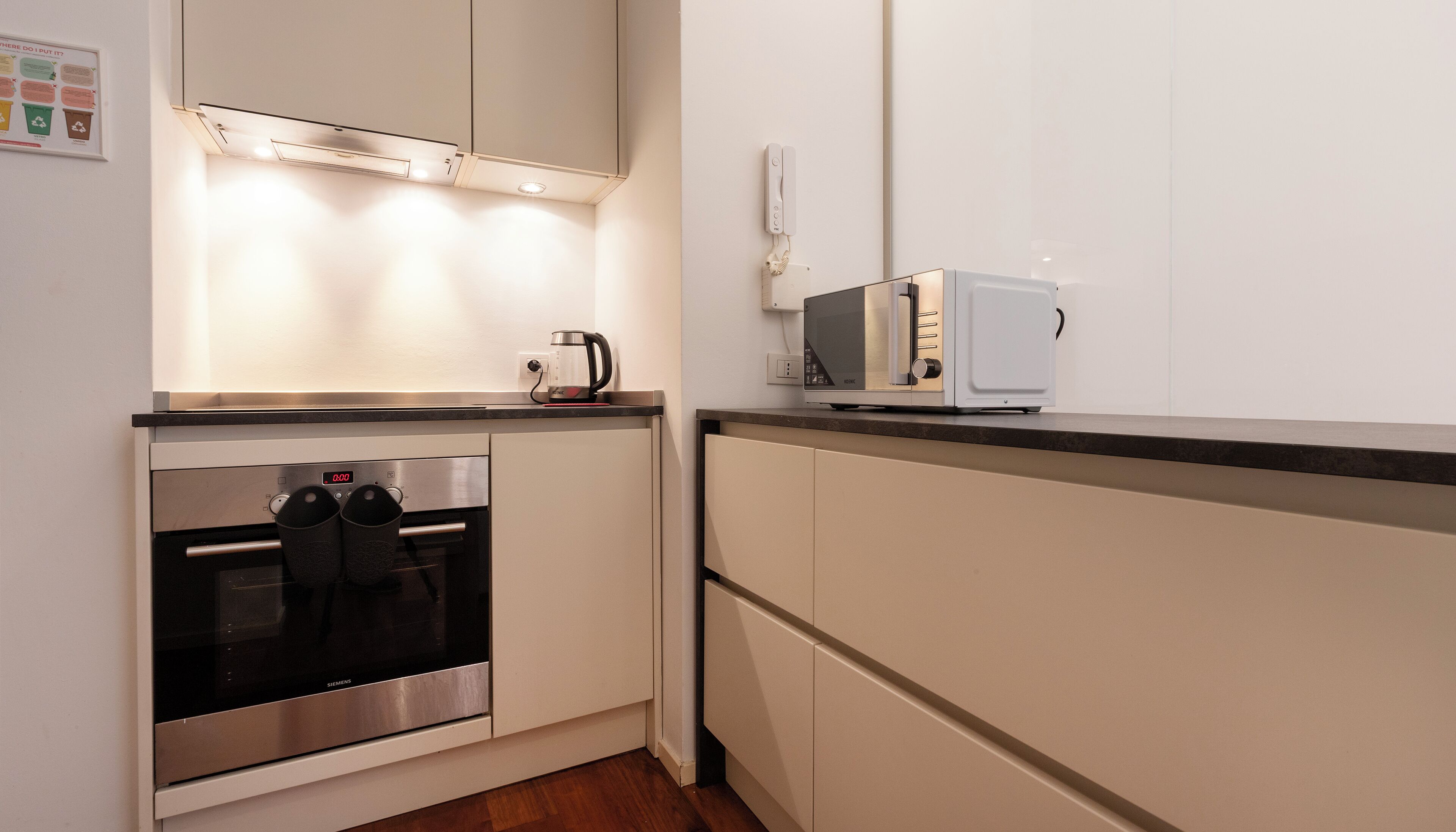 Una cocina moderna con horno empotrado, microondas y hervidor sobre la encimera.