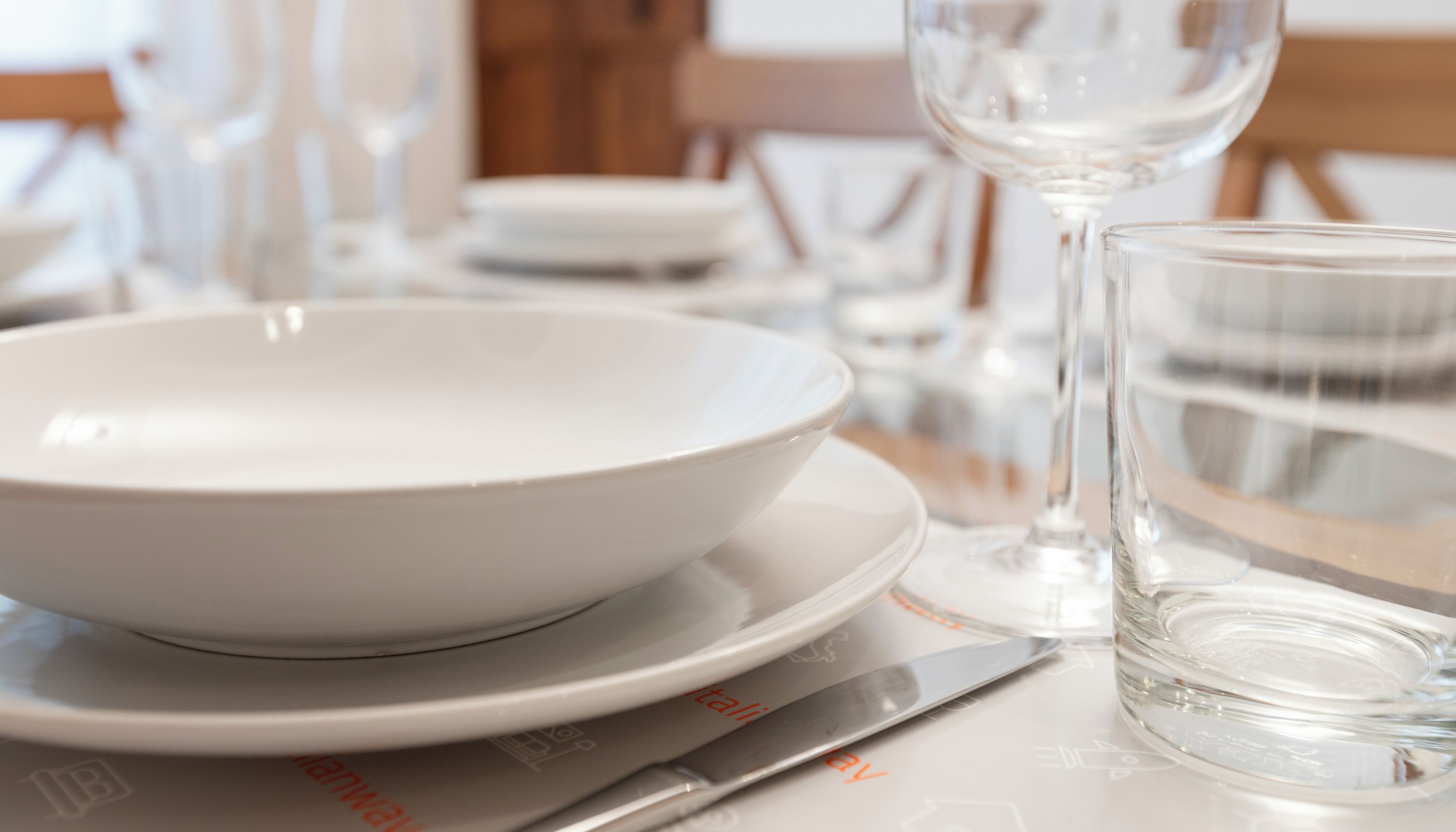 A dining table with a white bowl, a glass, and a knife.