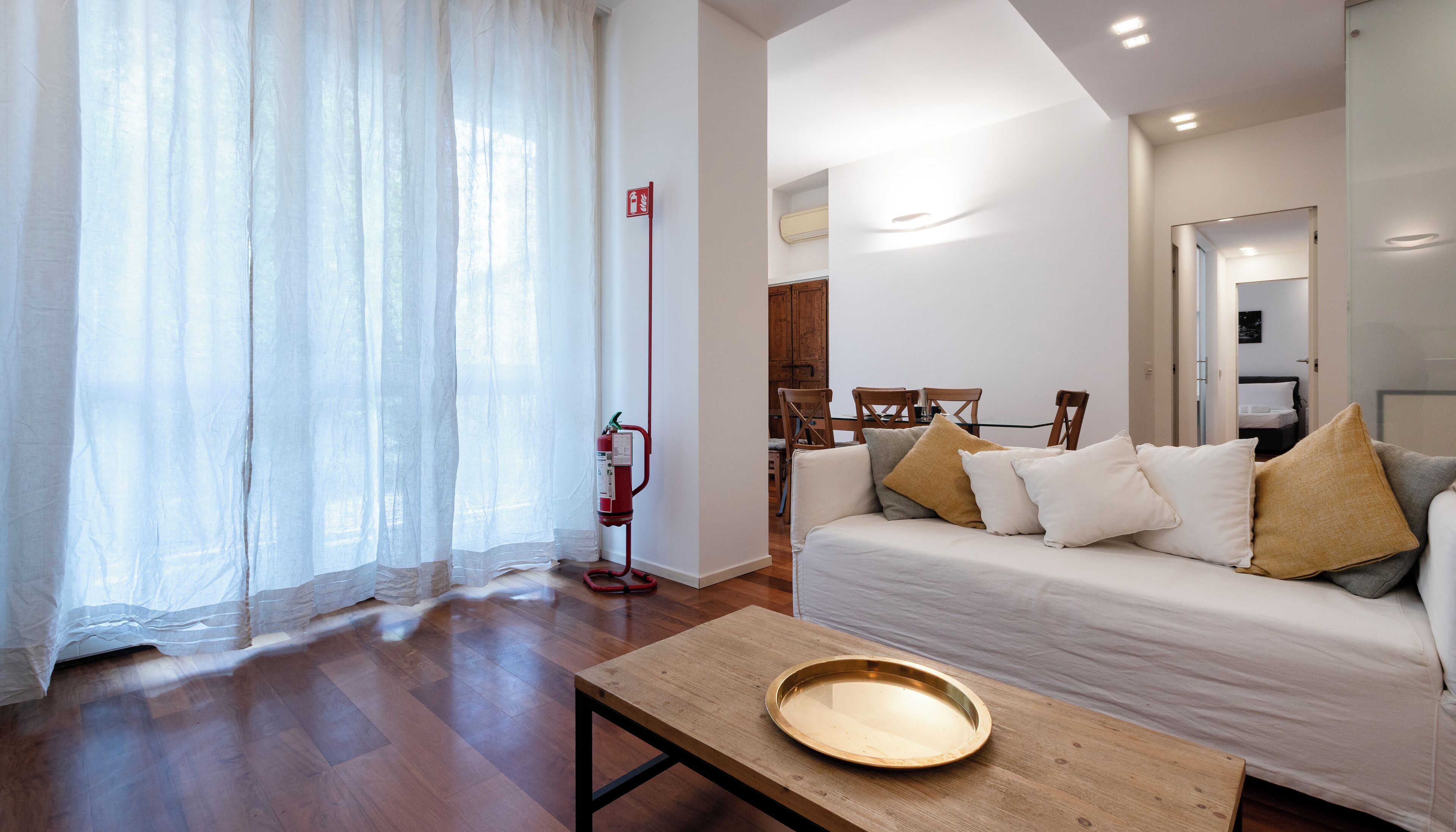 A modern living room with a sofa, a wooden table, and a fire extinguisher.