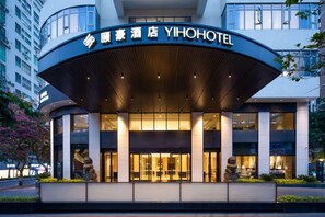 L'ingresso di un hotel moderno con una facciata curva, ampie vetrate e un cartello ben visibile.