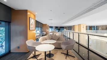 A modern lounge area with seating and tables, a glass railing, and a view of the outdoors.