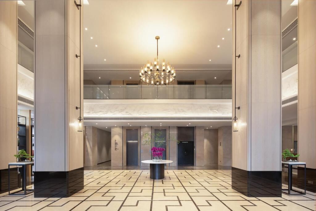 A hotel lobby with a geometric patterned floor, a central chandelier, and a mezzanine level.