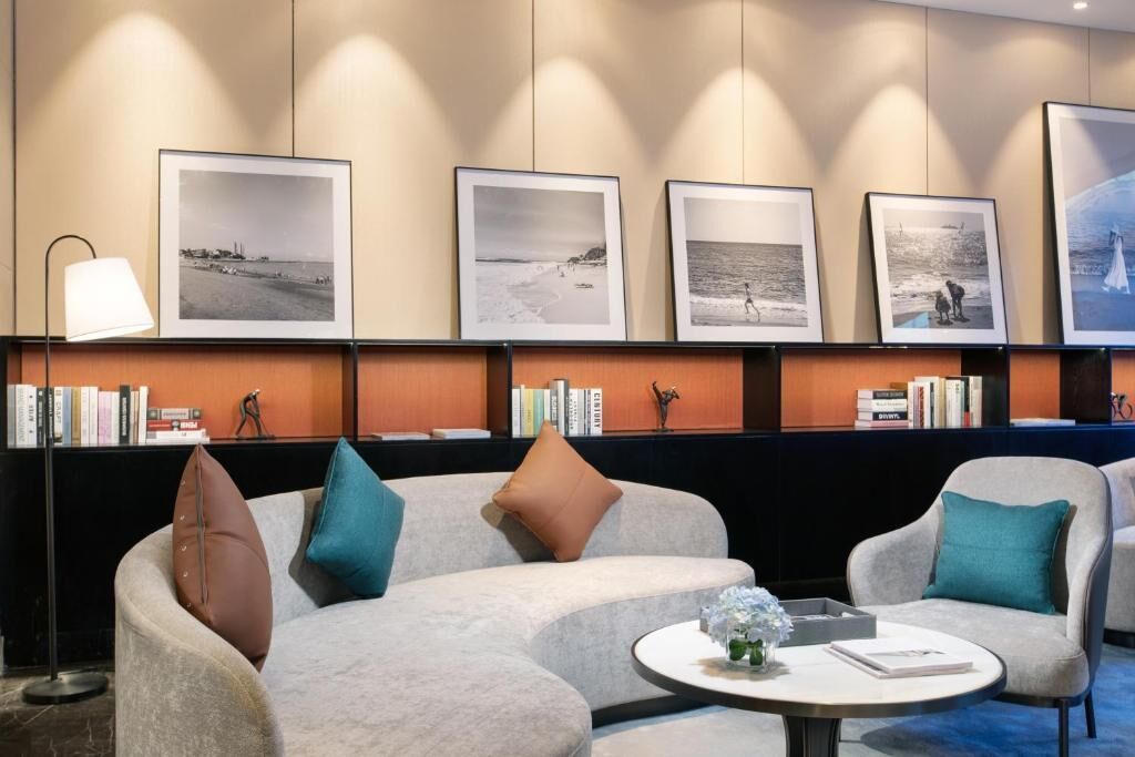 A modern lounge area with a curved sofa, armchairs, a round coffee table, and a bookshelf with framed photographs.