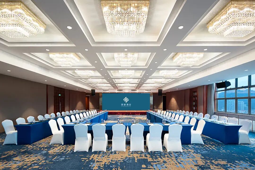 A conference room with a long table, white chairs, and chandeliers.