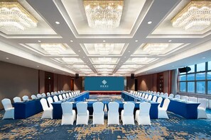 Un salón de conferencias con una larga mesa, sillas blancas y candelabros.