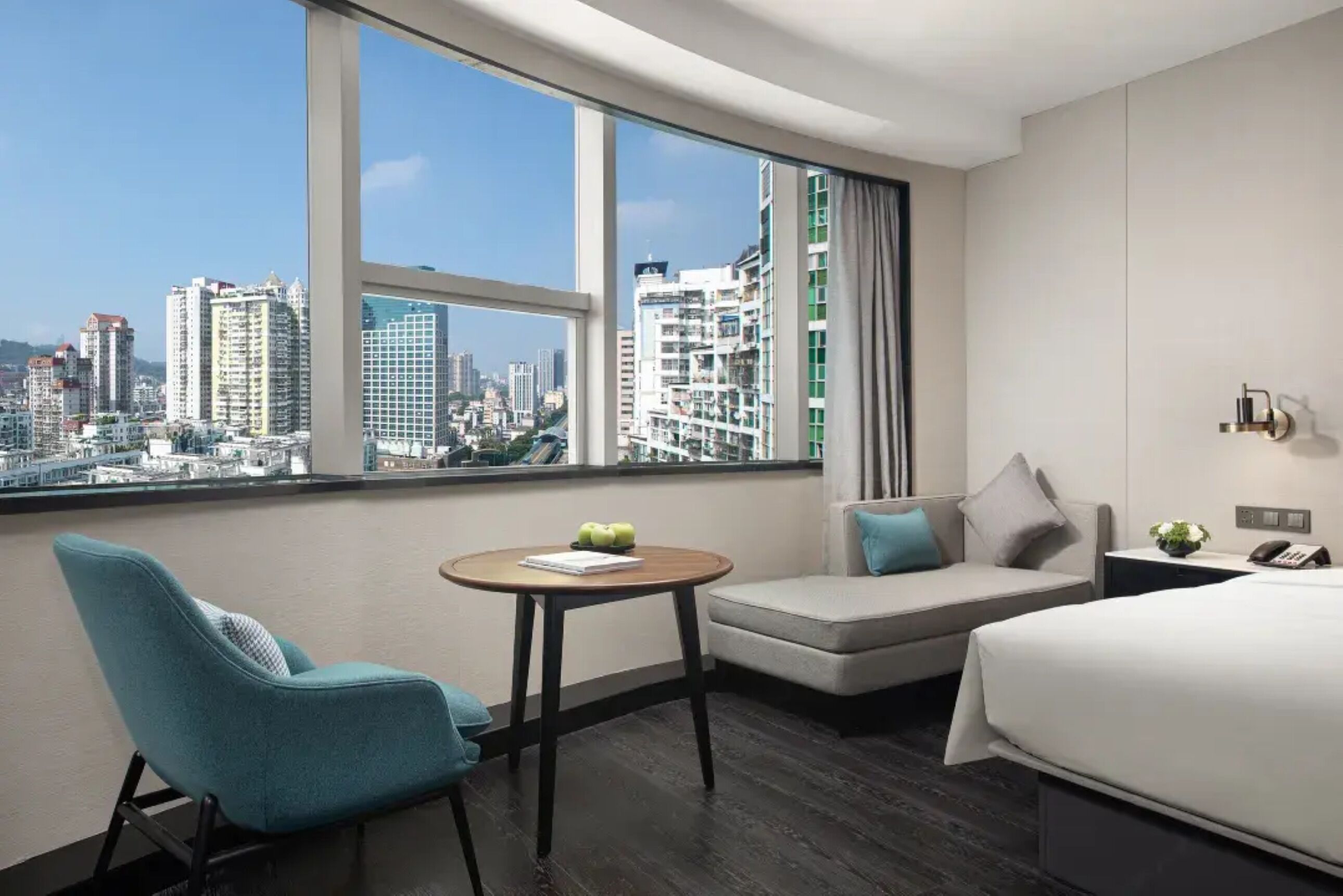 A hotel room with a city view, a sofa, a chair, a small table, and a bed.