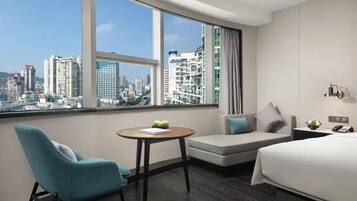 A hotel room with a city view, a sofa, a chair, a small table, and a bed.