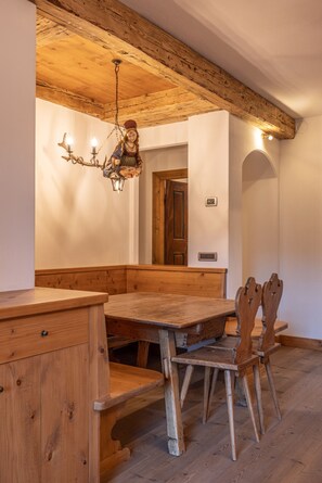 Ein Essbereich mit Holzboden, einer Bank und Stühlen, einer Kronleuchter und einer Holzkονtzession.