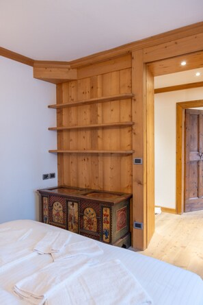 A bedroom with a wooden wardrobe, a bed with white linens, and a decorative chest of drawers. - Casa Ampezzo, in the town center with balcony and parking area (Cortina d´Ampezzo)