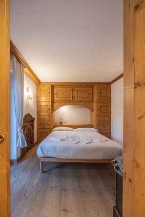 A bedroom with a wooden headboard, a bed with white linens, and a wooden wardrobe. - Casa Ampezzo, in the town center with balcony and parking area (Cortina d´Ampezzo)