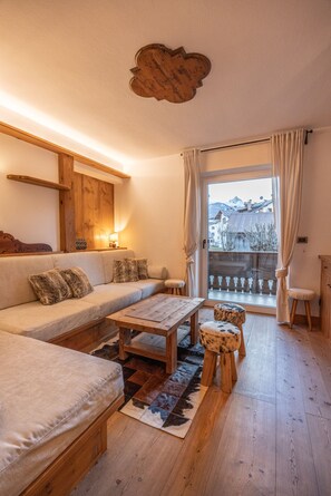 Ein gemütliches Wohnzimmer mit einer Couch, einem Holztisch und Blick auf eine Berglandschaft durch ein großes Fenster.