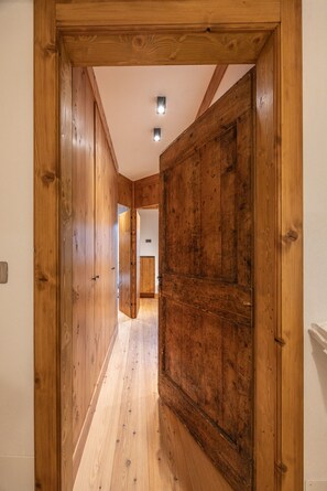 A wooden hallway with a door at the end, a ceiling light, and a visible electrical outlet on the wall. - Casa Ampezzo, in the town center with balcony and parking area (Cortina d´Ampezzo)