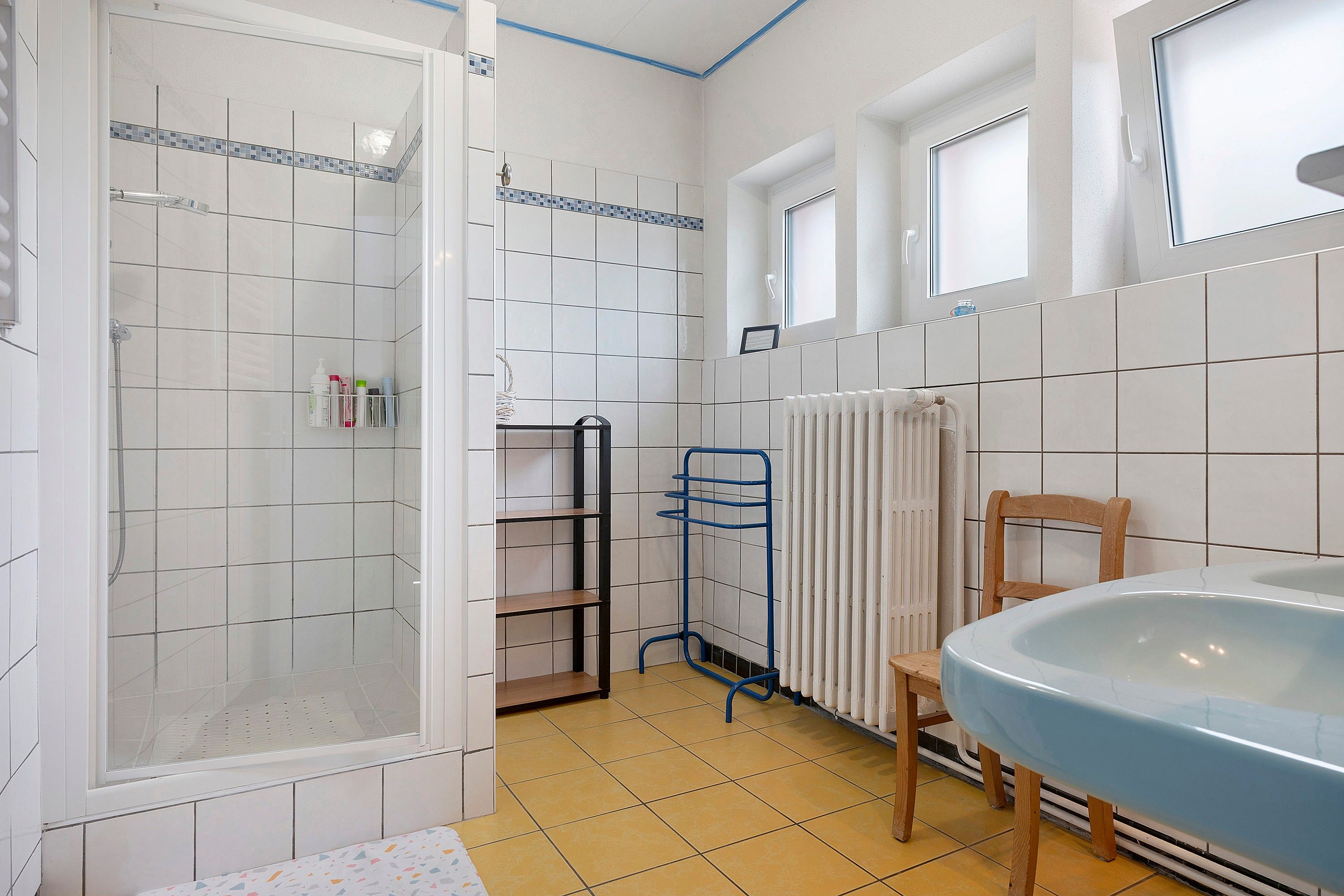 Une salle de bain avec une douche, un lavabo, une chaise et un radiateur.