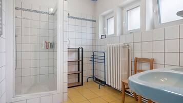 Een badkamer met een douche, wastafel, stoel en radiator.