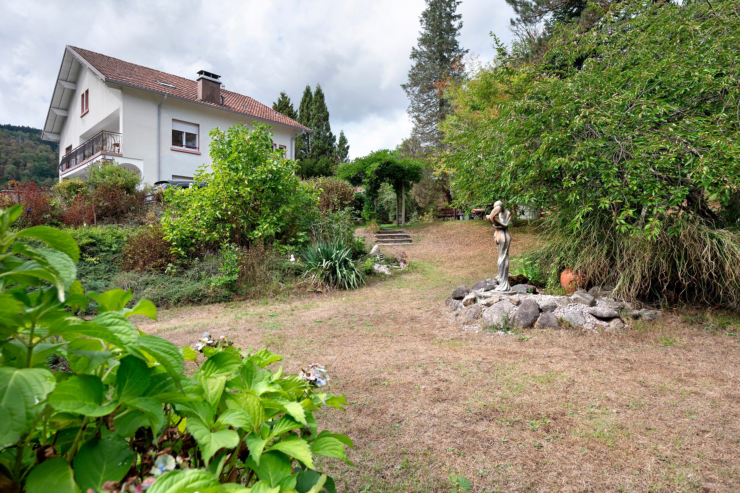 Ein Haus mit Garten, einer Statue und Blick auf einen Hügel.