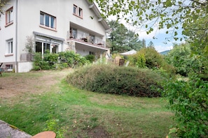 En toetagers bygning med balkon, omgivet af grøn vegetation og en have.