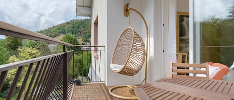 A balcony with a hanging chair, a table, and a view of a hillside.