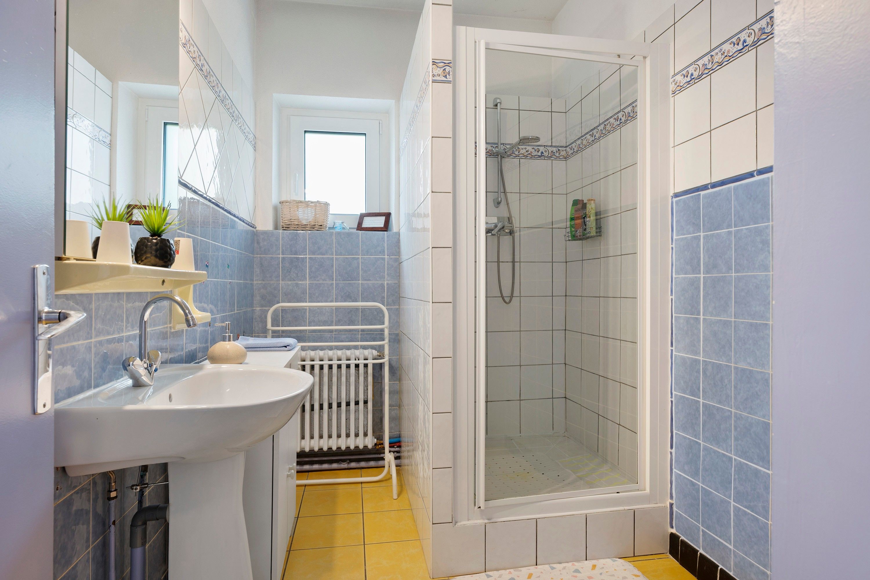 Een badkamer met een wastafel, spiegel, douche en betegelde wanden.