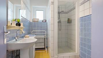Een badkamer met een wastafel, spiegel, douche en betegelde wanden.