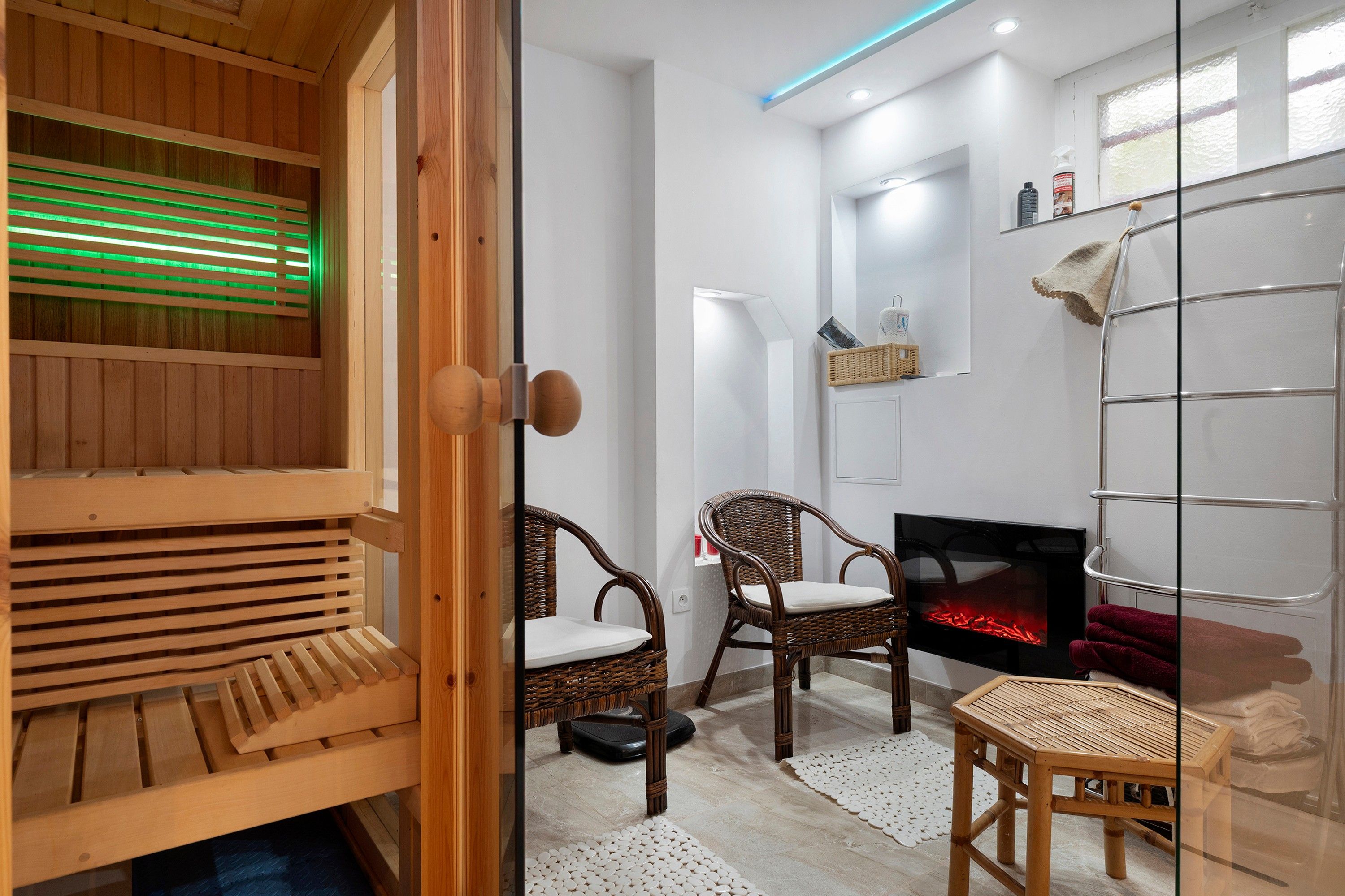 Un sauna avec des bancs en bois, un fauteuil en osier, une petite table et une cheminée.