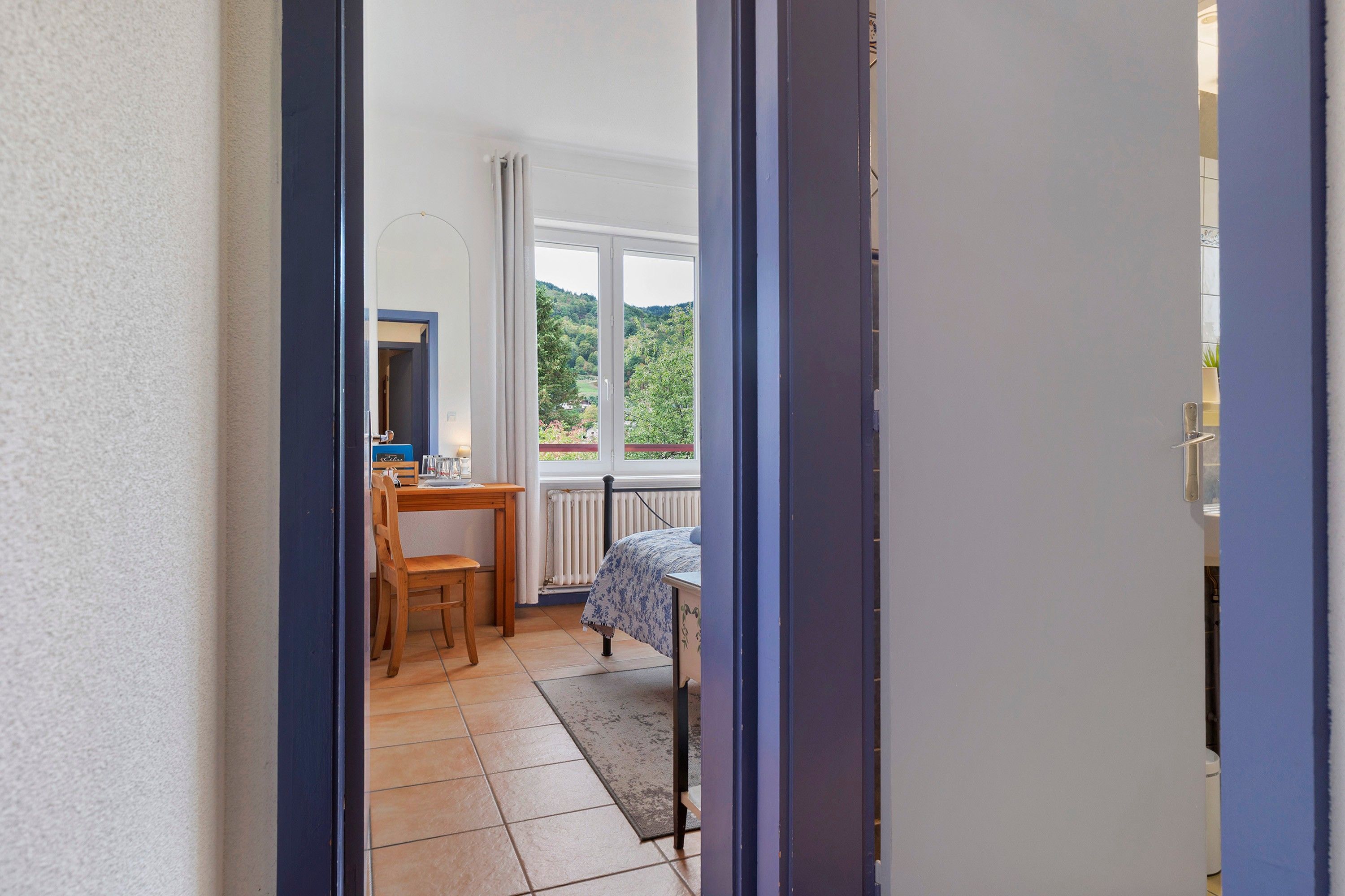 Une pièce comprenant un lit, une table et une chaise. Il y a une fenêtre donnant sur un paysage verdoyant.