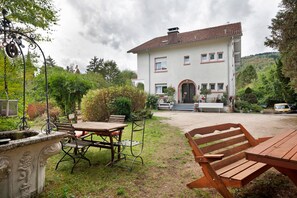 A two-story house with a garden patio, a dining table, and outdoor seating.
