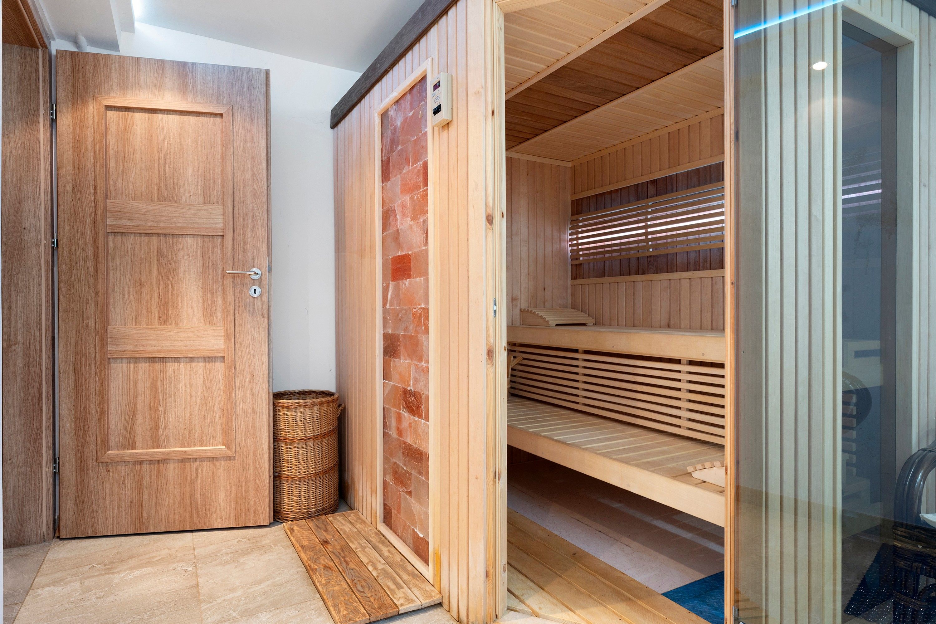 A wooden door with a keyhole and a handle, a wicker basket, and a sauna with benches and a glass door.