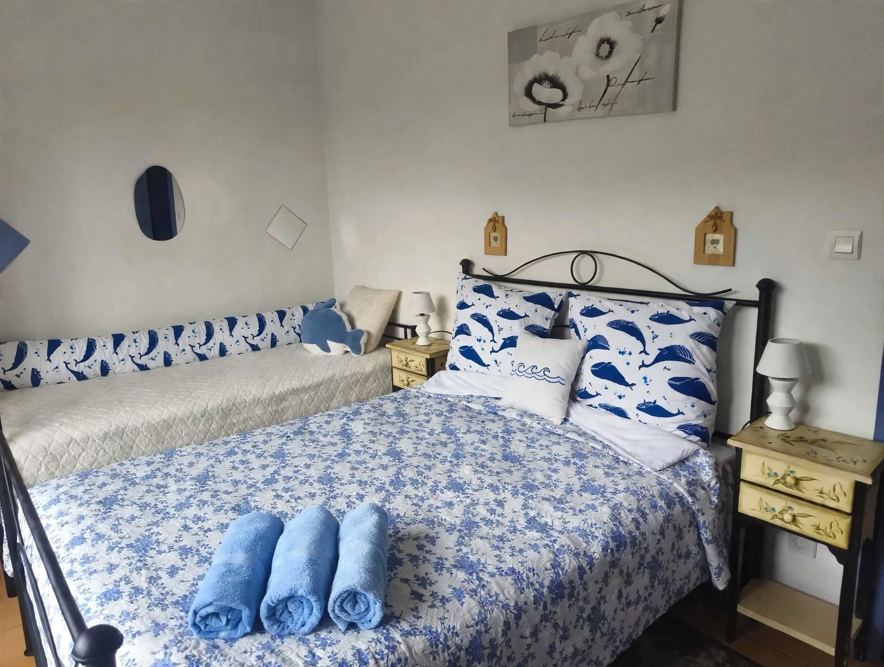 A double bed with floral bedding, two pillows with a blue whale pattern, and a pair of rolled towels.