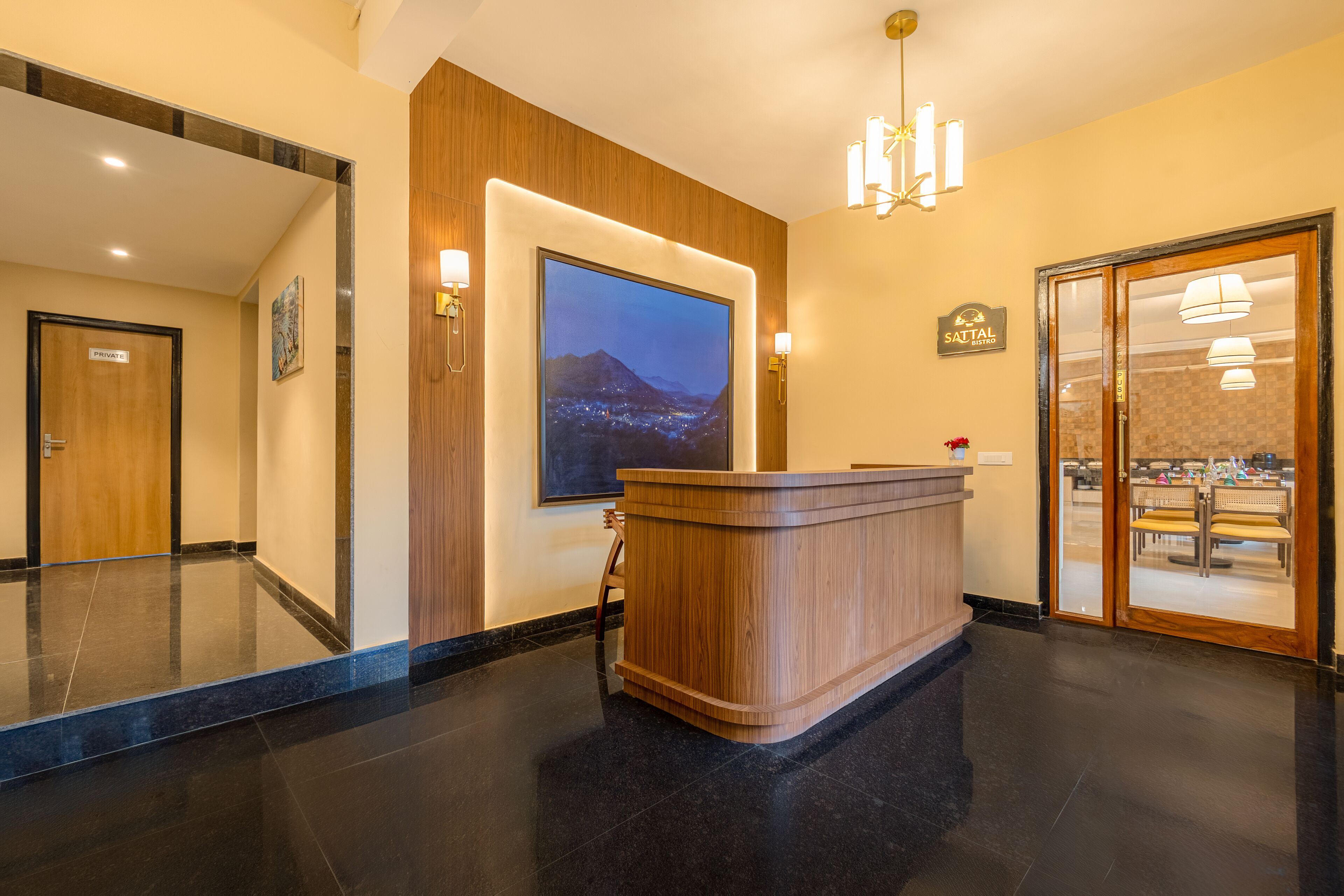 Ein Hotel-Empfangsbereich mit einem Holzbüro, einem großen Stadtbild in einem Rahmen und einer Glastür zum Speisesaal.