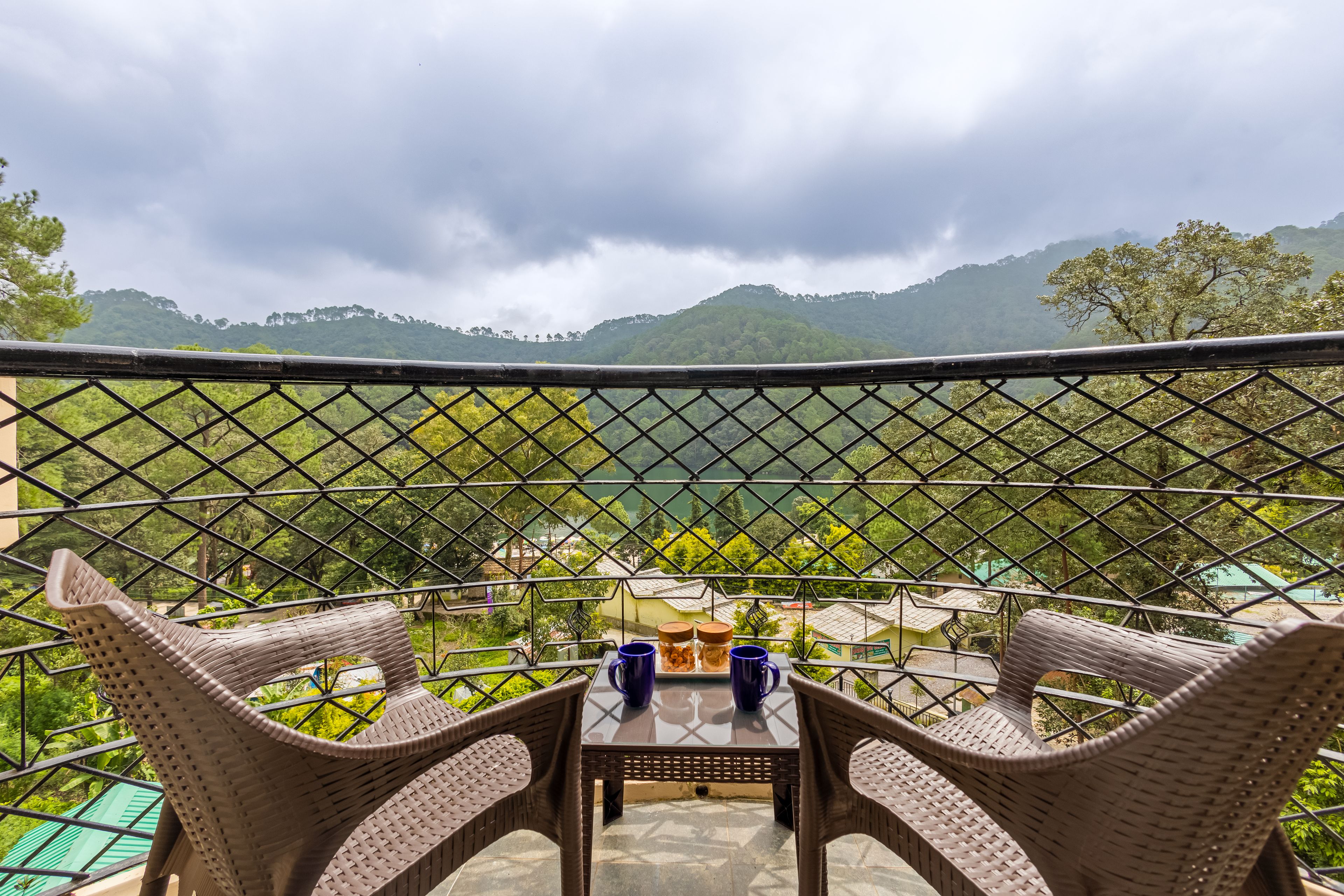 A balcony with wicker chairs and a table, overlooking a mountainous landscape.