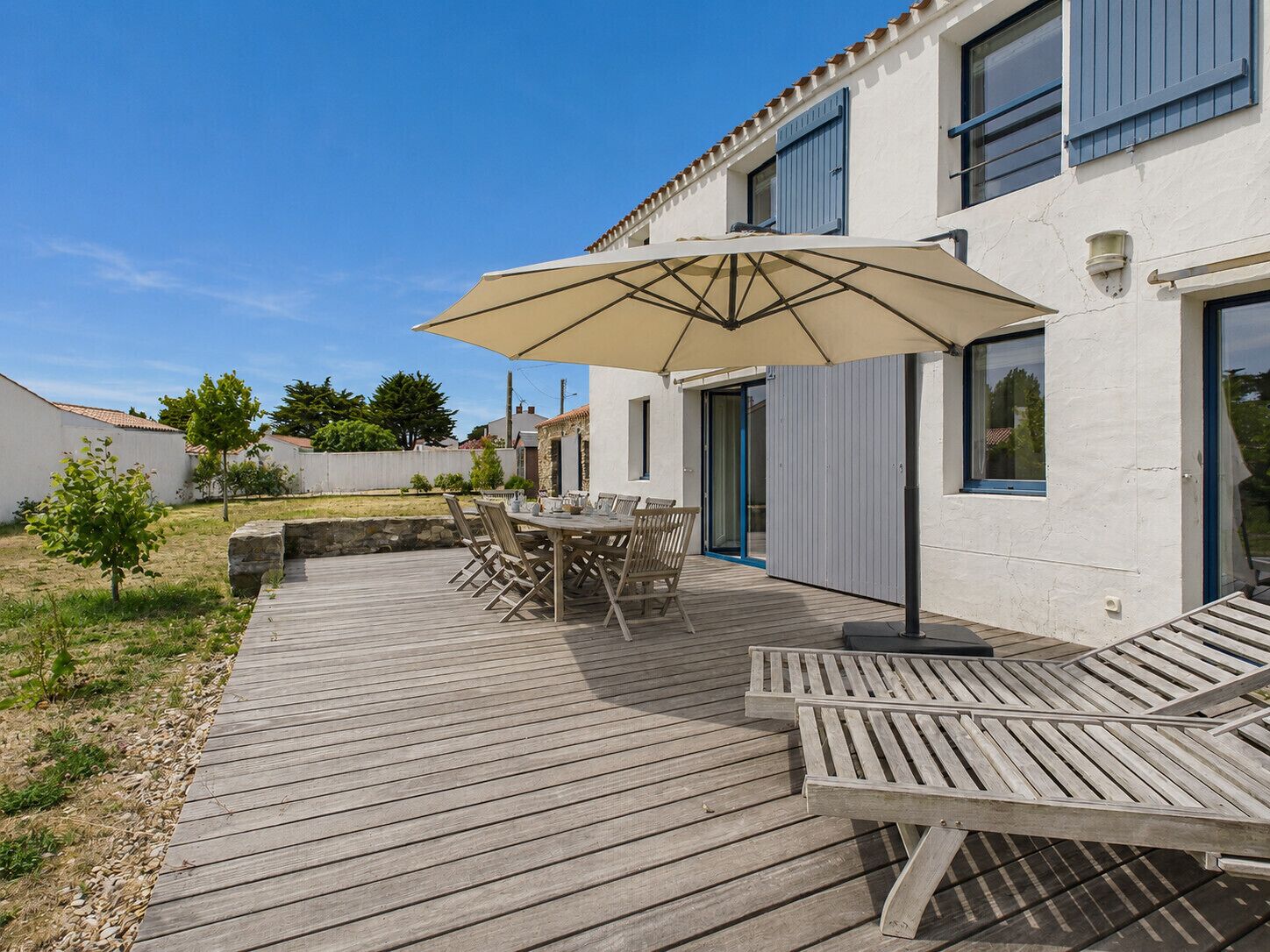 A wooden deck with a table and chairs, an umbrella, and a lounge chair.