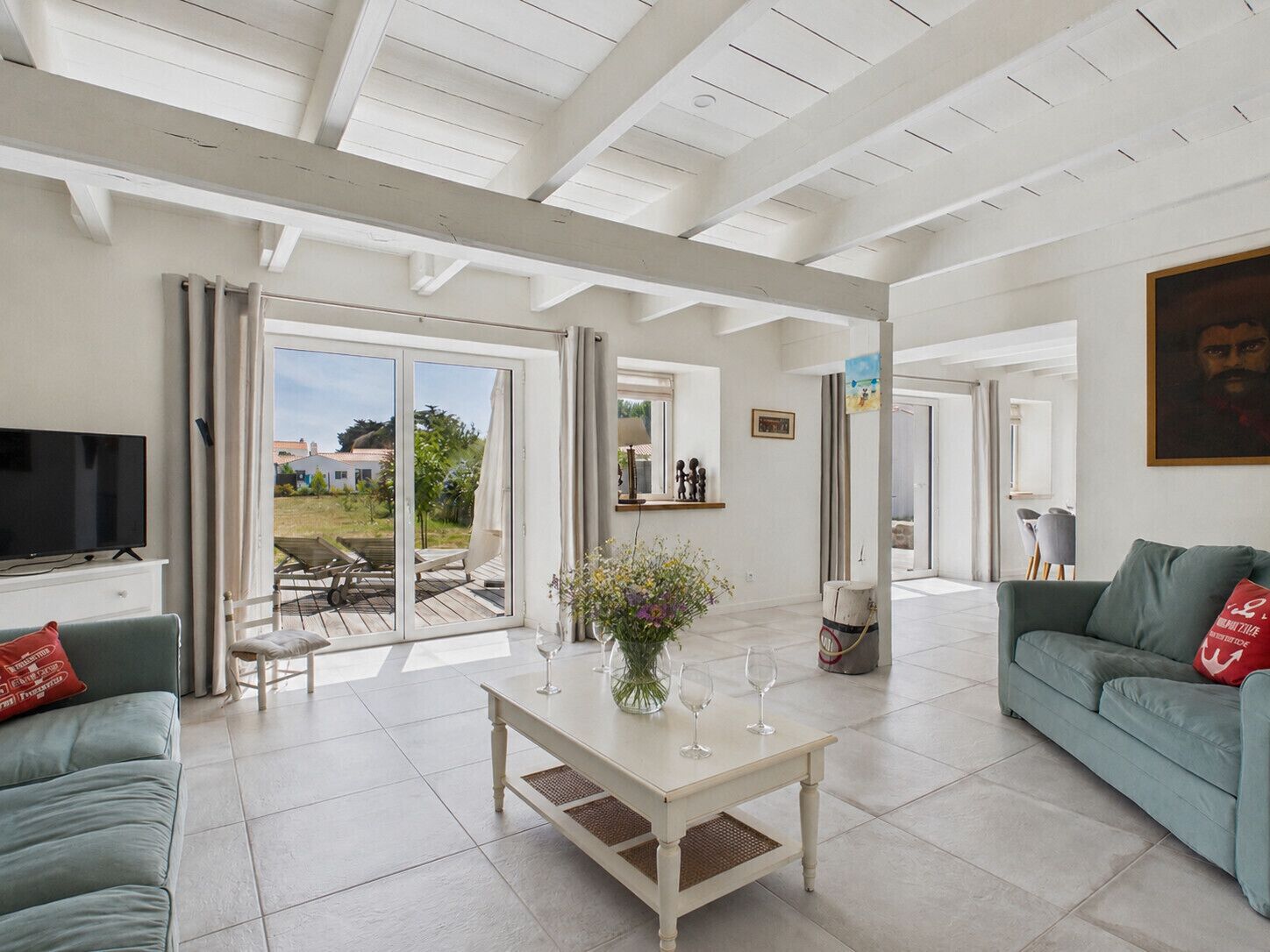 Un salón espacioso con televisor, un sofá, una mesa de centro con copas de vino y vistas a un patio exterior por una puerta de vidrio.