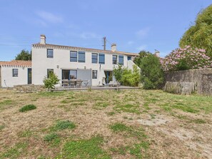 Ein zweigeschossiges Gebäude mit einer Terrassenfläche, einem kleinen Garten und einem Holzzaun.